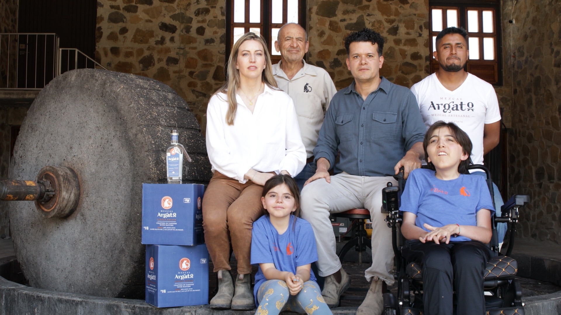 The Landa family at the Mezcal Argato distillery, gathered beside the volcanic stone tahona wheel with cases of Argato Espadín
